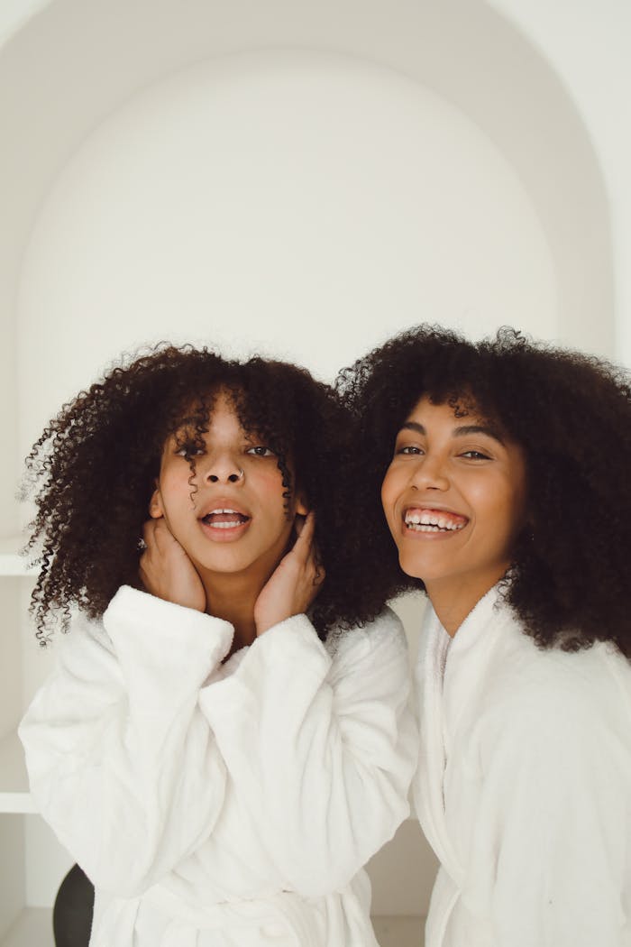 Two smiling women with afro hair in bathrobes, embodying relaxation and friendship.