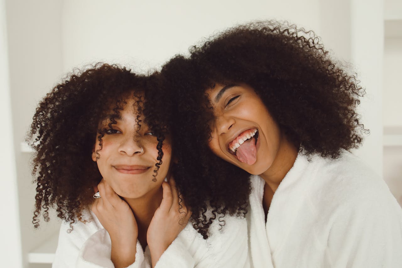 Two happy African American women with curly hair wearing bathrobes, expressing joy indoors.