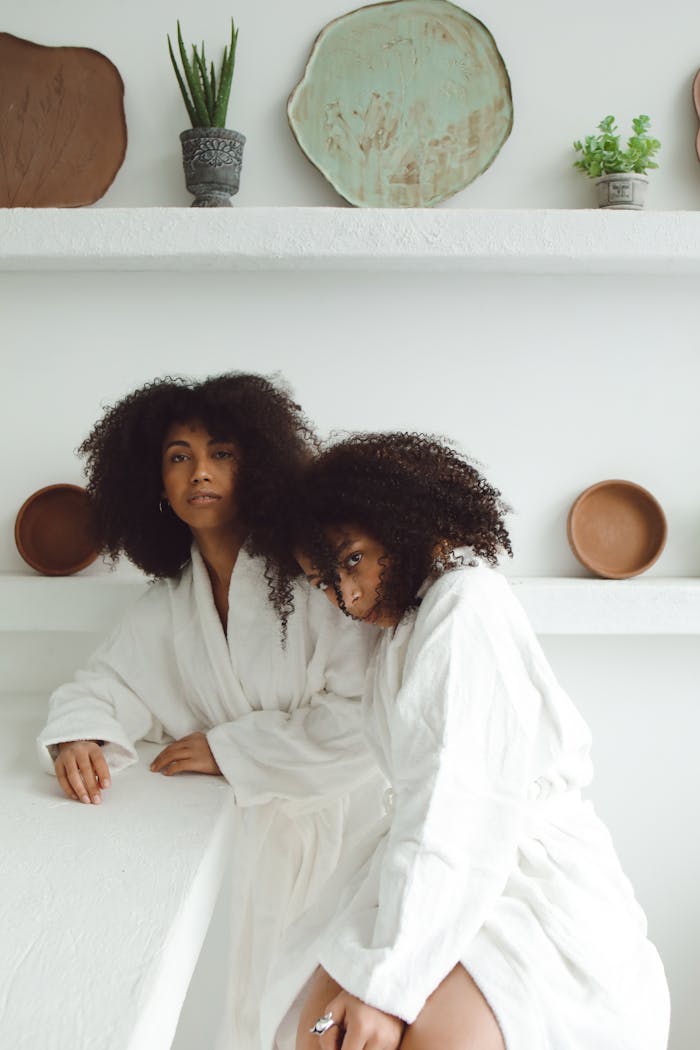 Two women in white robes with natural curls in a serene spa setting, embodying relaxation and elegance.