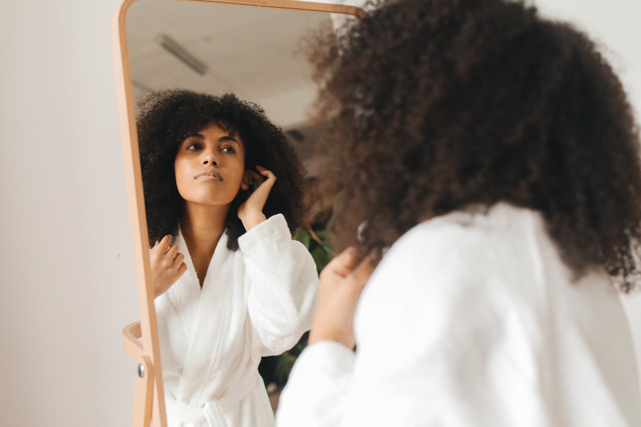 Woman in bathrobe with curly hair looks at herself in mirror, getting ready.