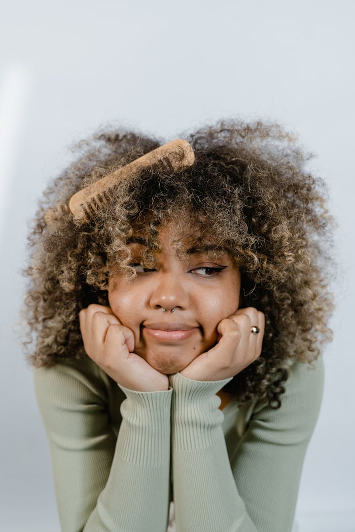 Thoughtful woman with curly hair posing with hands under chin and wooden comb.